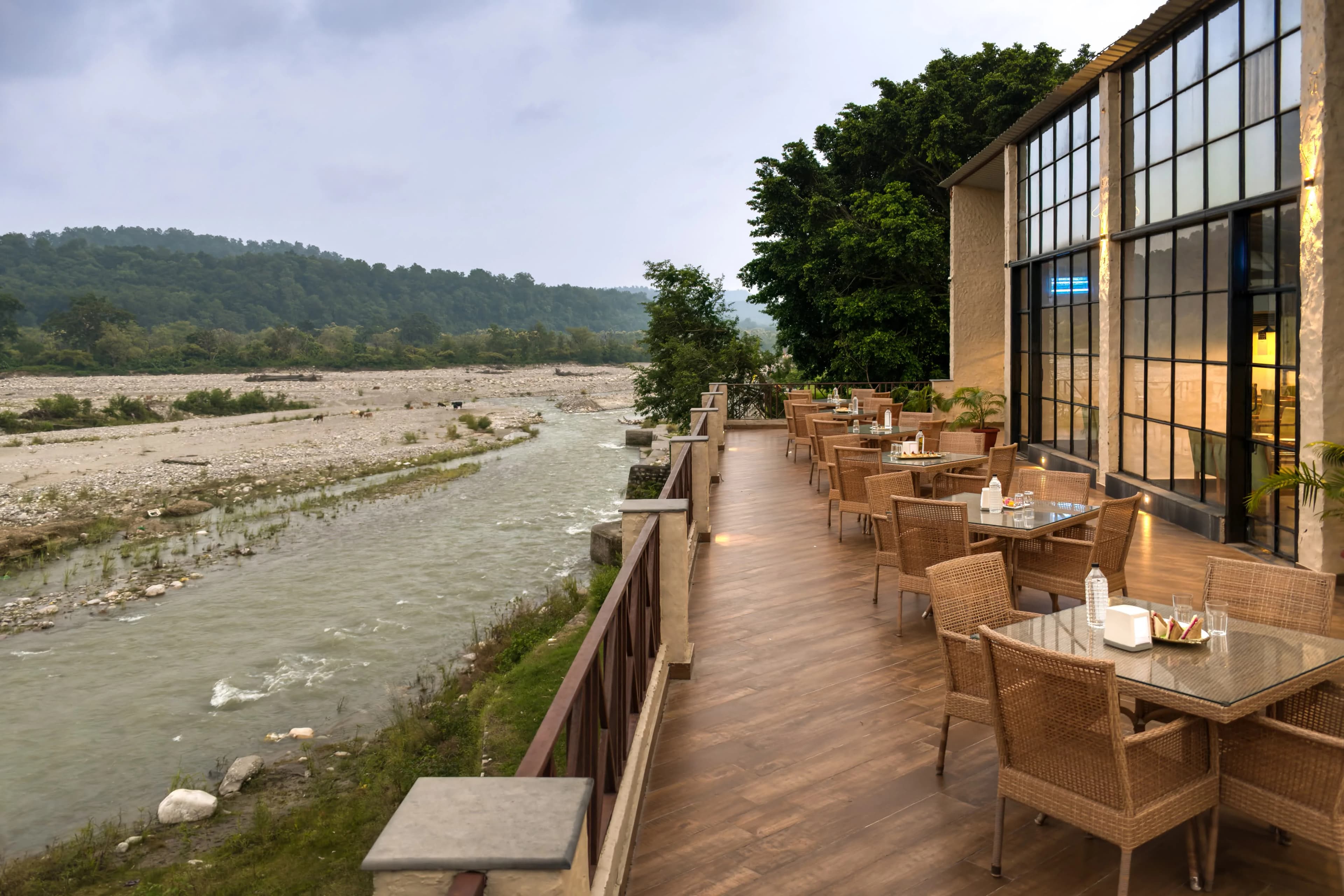 Riverside resort building with large glass windows and an outdoor balcony overlooking a wide, rocky riverbed.